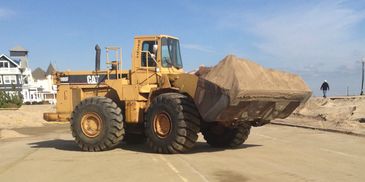 Yellow CAT 980F loader carrying sand at a construction site near houses.
