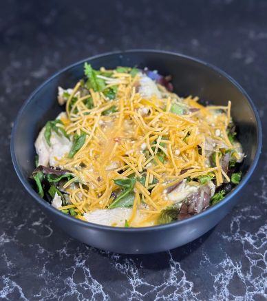 Salad with shredded cheese and greens in a black bowl.