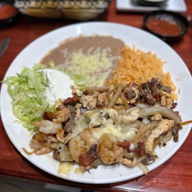 Plate with shrimp, chicken, beef, rice, beans, lettuce, and sour cream.