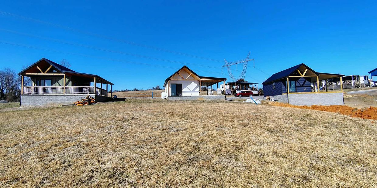 Three small houses on a grassy hill under a clear blue sky.