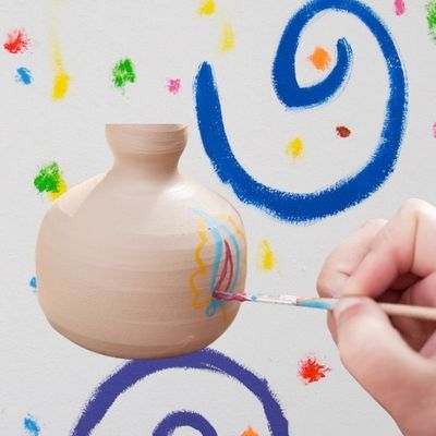 Hand painting colorful designs on a beige ceramic vase.