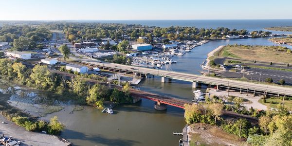 Aerial view of a coastal town with bridges, boats, and greenery under clear skies.