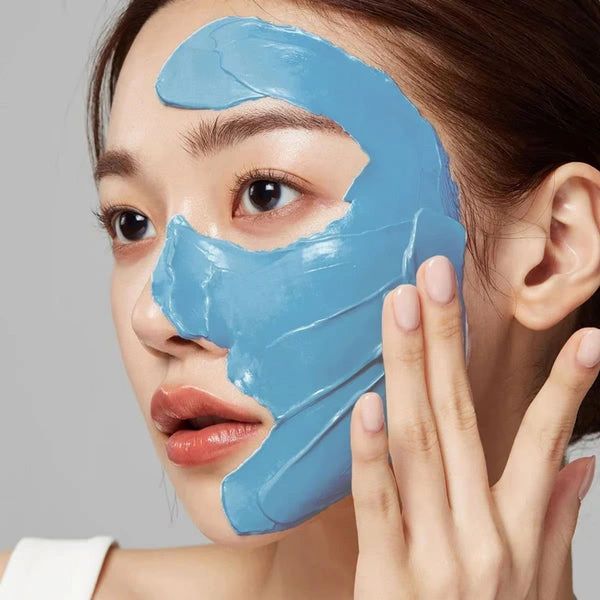 Woman applying a blue facial mask to her face.