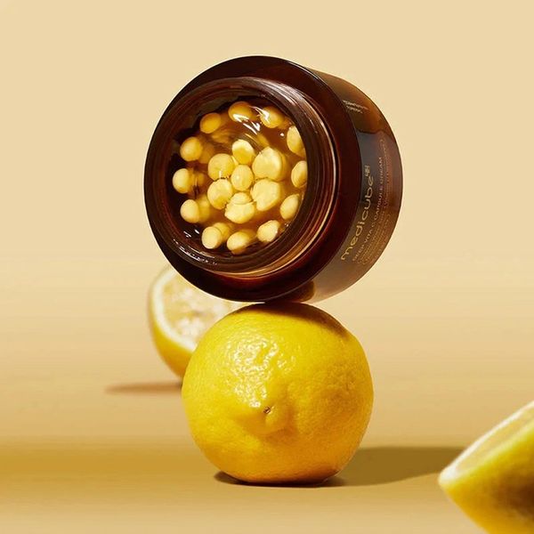 A skincare jar filled with yellow capsules balanced on a lemon.