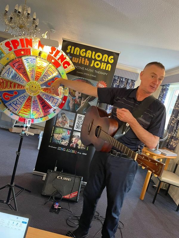 Man with guitar spinning a colorful prize wheel indoors.