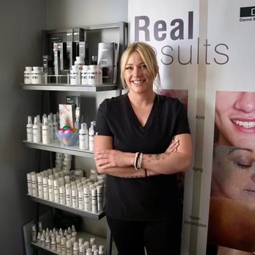 Esthetician Kitty Williams standing in front of a shelf that is displaying DMK skincare products.