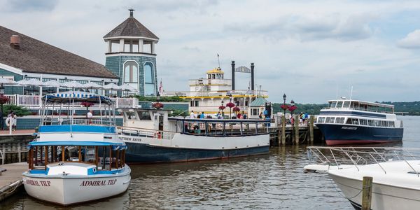 Several boats docked at a waterfront with a lighthouse-style building in the background.