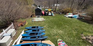 Kayaks and paddleboards are neatly arranged outdoors on a lawn.