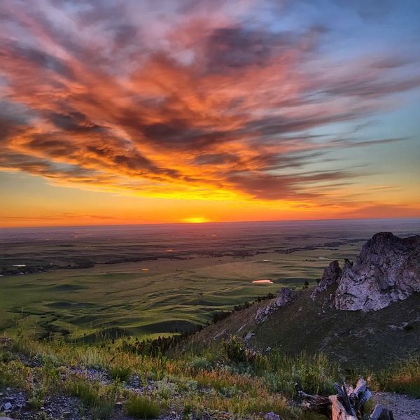 Sunset over a vast green landscape with rocky hills.