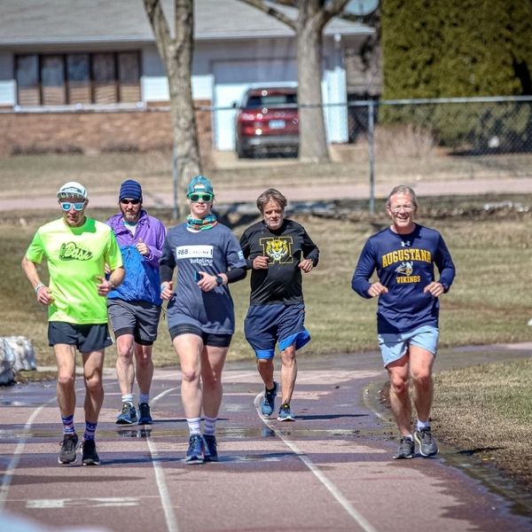 Five adults jogging together on an outdoor track on a sunny day.
