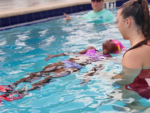 Child learning to float in swimming pool with instructor.