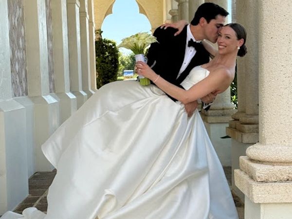 Groom kissing bride while holding her in wedding dress.