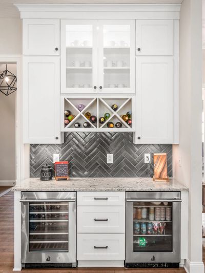 Modern kitchen bar area with white cabinets and wine storage.