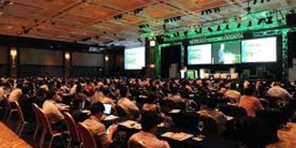 Large audience attending a conference in a spacious hall with presentations.