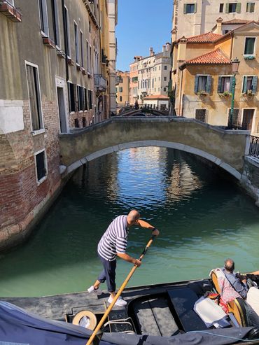 A gondolier navigating a narrow canal under a stone bridge in Venice.