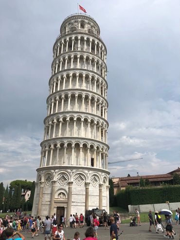 The Leaning Tower of Pisa with tourists around it on a cloudy day.