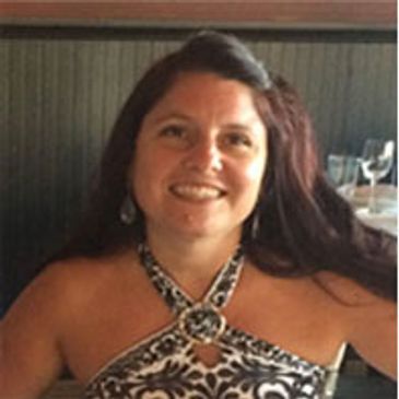 Smiling woman with long dark hair in a patterned halter dress.
