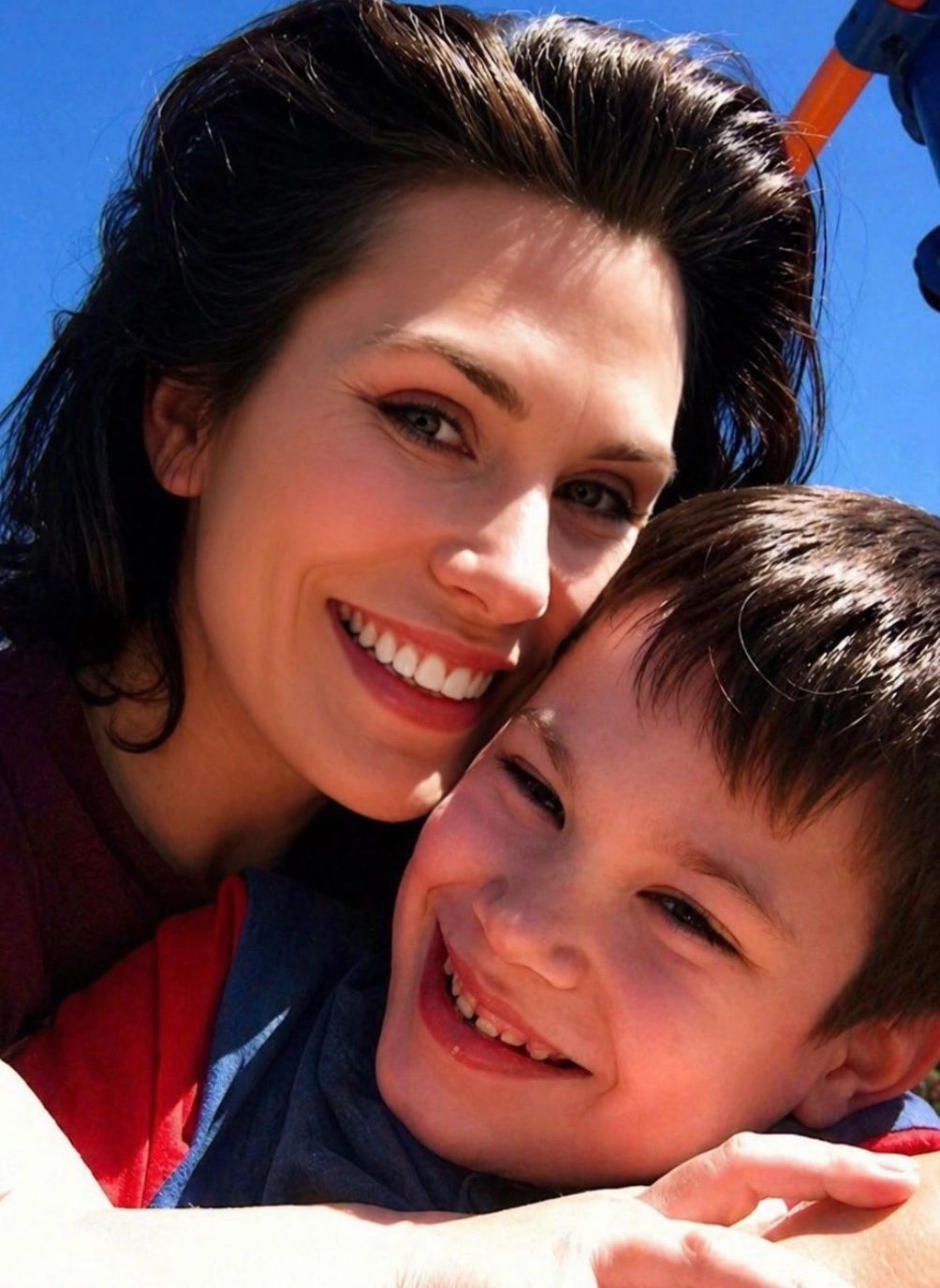 A joyful mother and son smiling closely together outdoors.