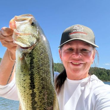 Woman proudly holding a large fish she caught by the lake.