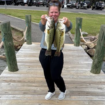 Woman proudly holding two large fish on a wooden dock.