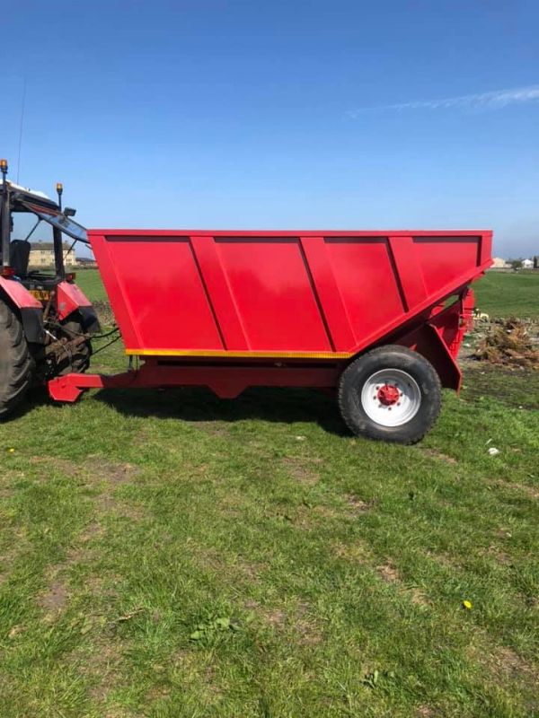 Red agricultural trailer attached to a tractor on grass.