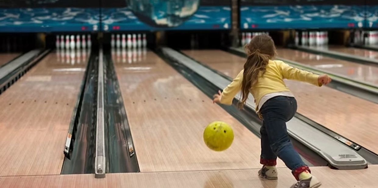 A child bowls with a yellow ball at a bowling alley.