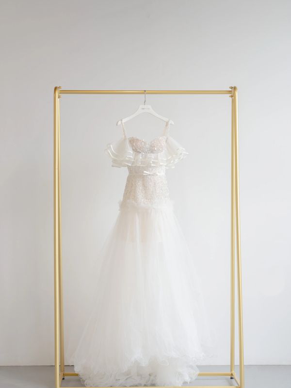 Elegant white wedding dress with lace and tulle details hanging on a gold rack.
