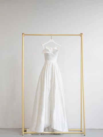 Elegant white strapless gown hanging on a minimalist gold rack.