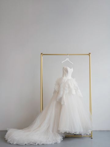 Elegant white wedding dress with a long train on a gold rack.
