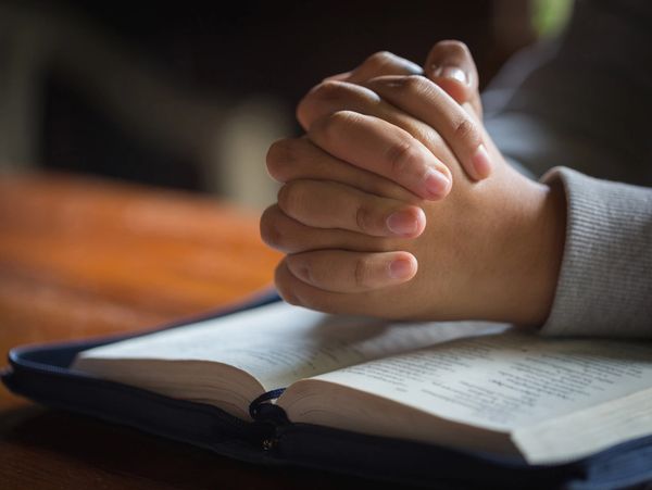 Person's hands clasped in prayer over the bible.