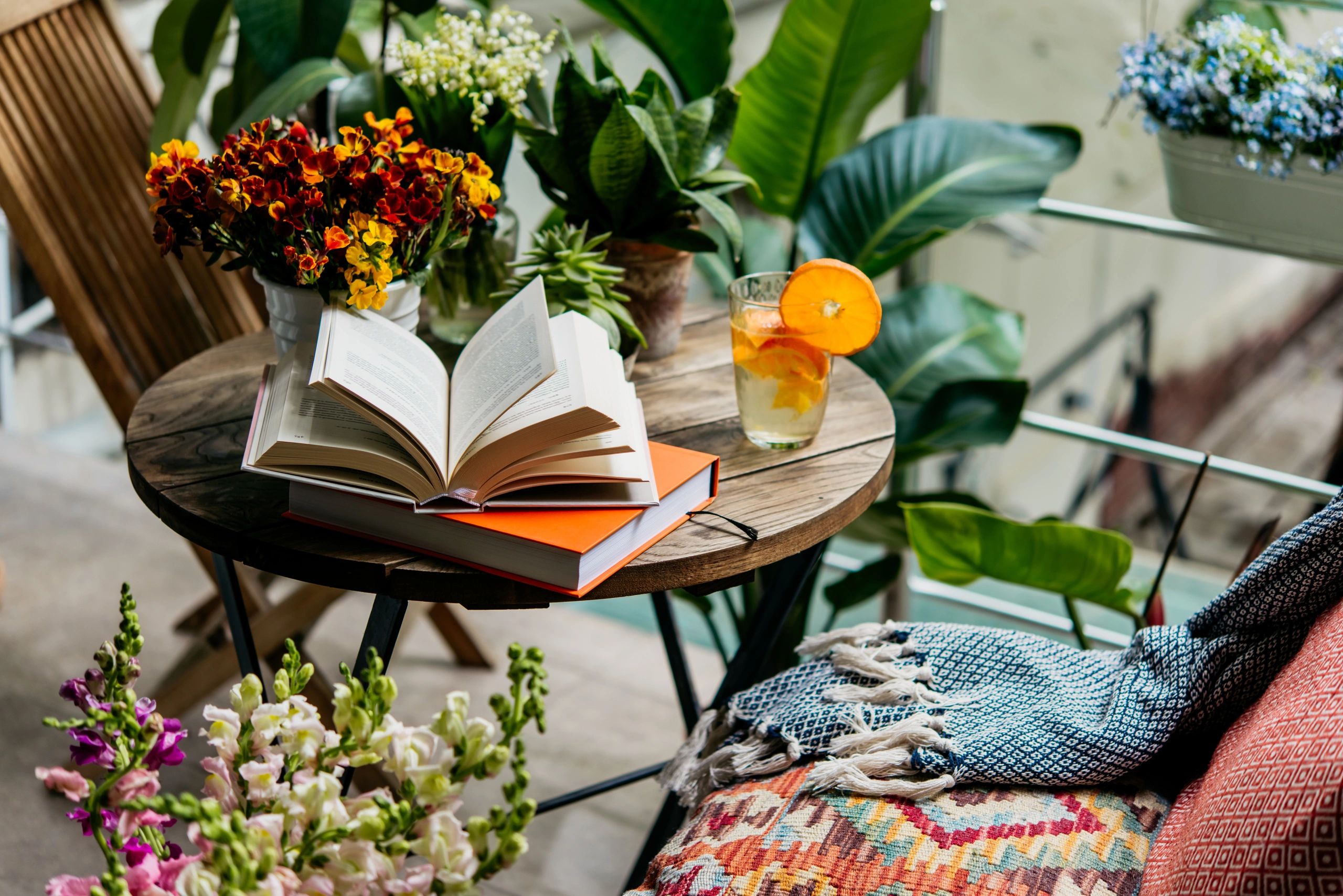 Cozy reading nook with an open book, vibrant flowers, and a refreshing citrus drink on a wooden table.