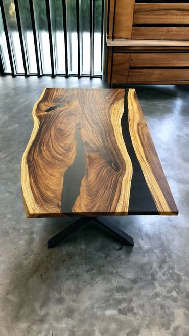 Elegant live edge wooden table with black resin inlay on a concrete floor.