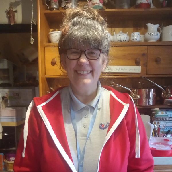 Smiling woman in glasses wearing a red jacket in a cozy kitchen.