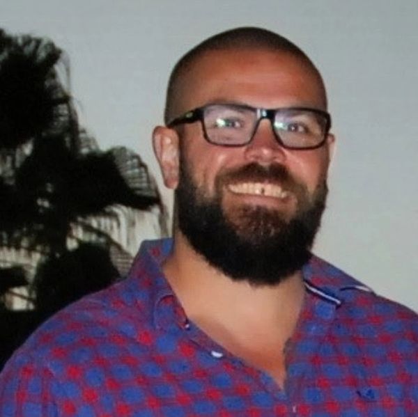 Smiling man with glasses and beard in a checkered shirt.