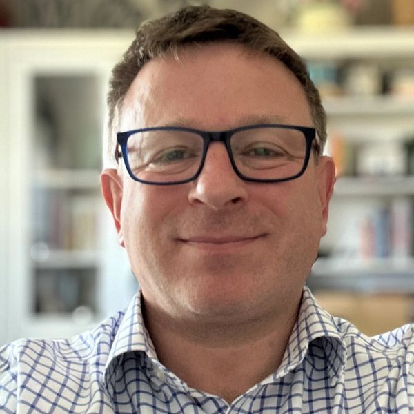 A man wearing glasses and a checkered shirt smiling.