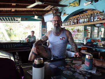Tattooed man sitting on a bar counter.