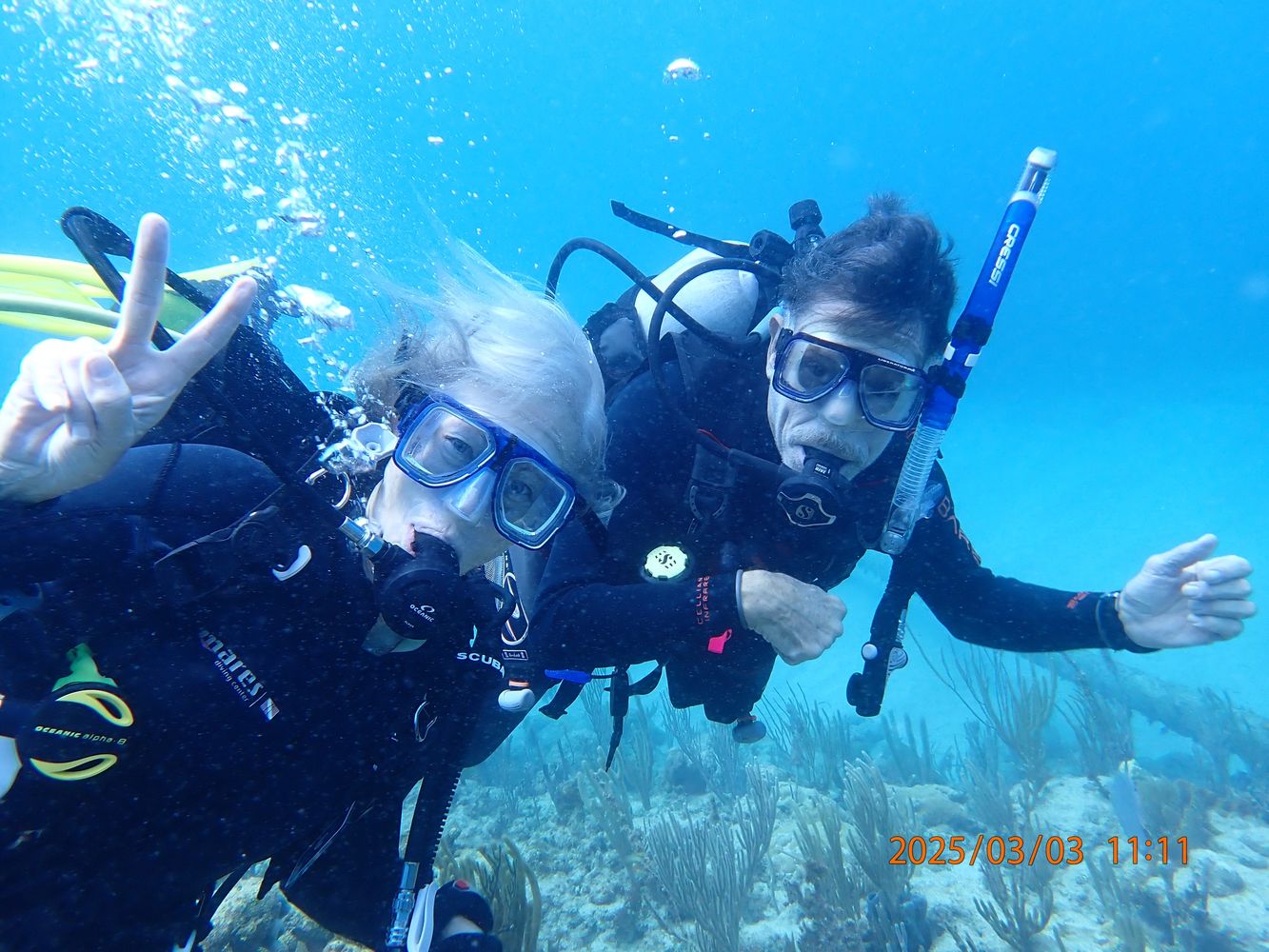Two scuba divers underwater with one showing a peace sign.