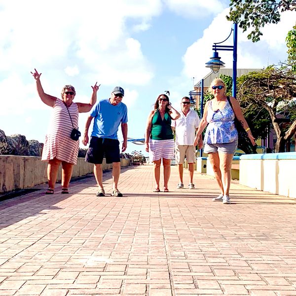 Group of five adults walking on a sunny promenade.