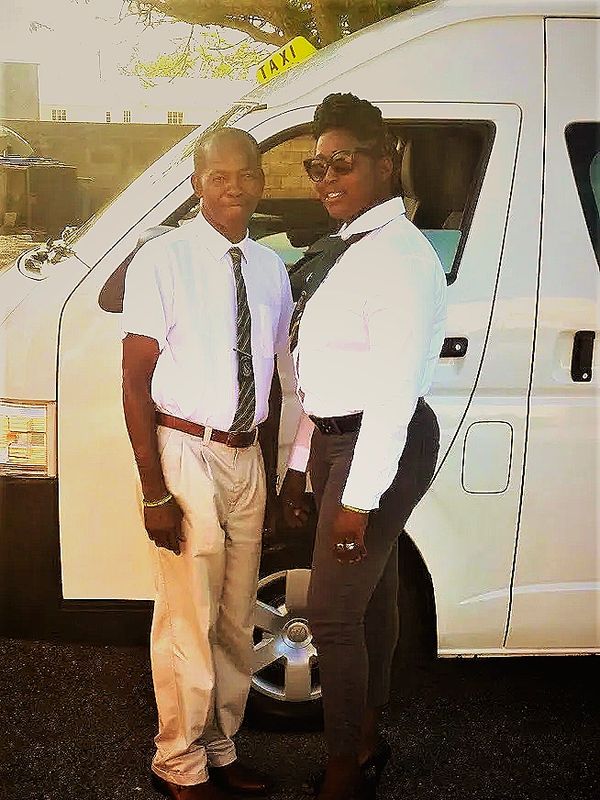 Two people in formal attire standing by a taxi van.
