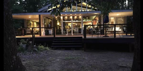 A warmly lit modern house exterior at dusk surrounded by trees.