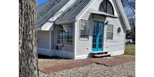 Small white house with blue door and gravel yard under clear sky.