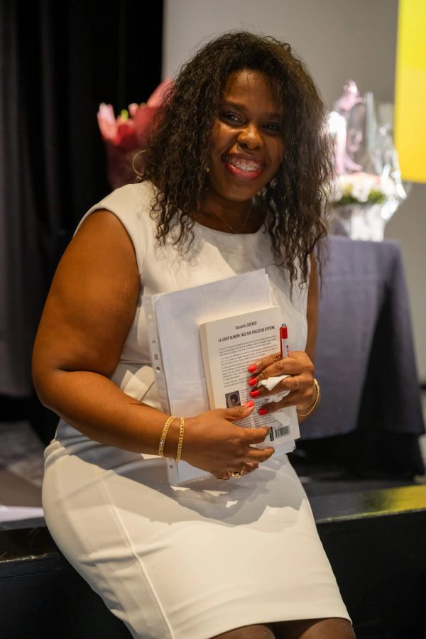 Smiling woman in white dress holding books and papers.