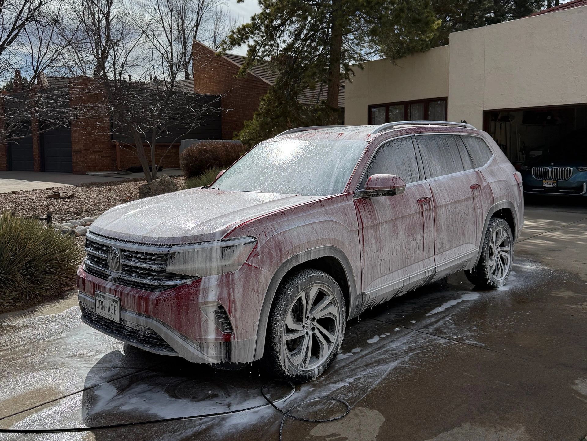 Red Volkswagen SUV covered in foam during a wash on a driveway.