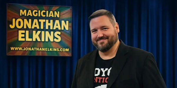Magician Jonathan Elkins posing with a promotional sign.