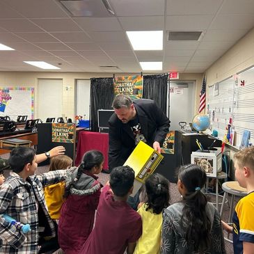 Magician Jonathan Elkins entertains a group of children with a magic trick in a classroom.