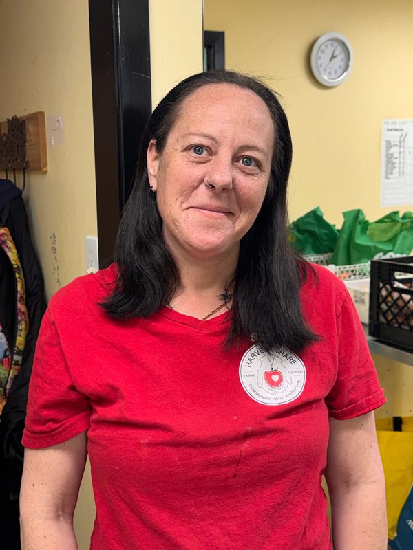 Woman in red shirt with a community food program logo smiles indoors.