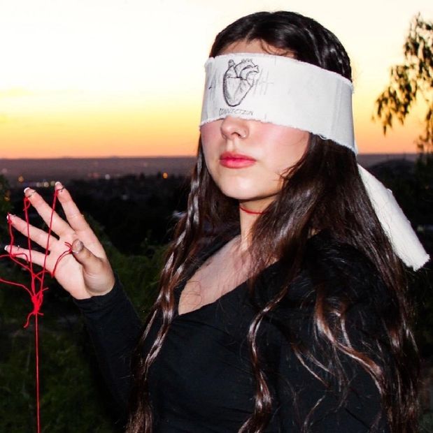 Pictured is the artist, Carolina (also known as Kako). Wearing a blindfold with a heart sketch.