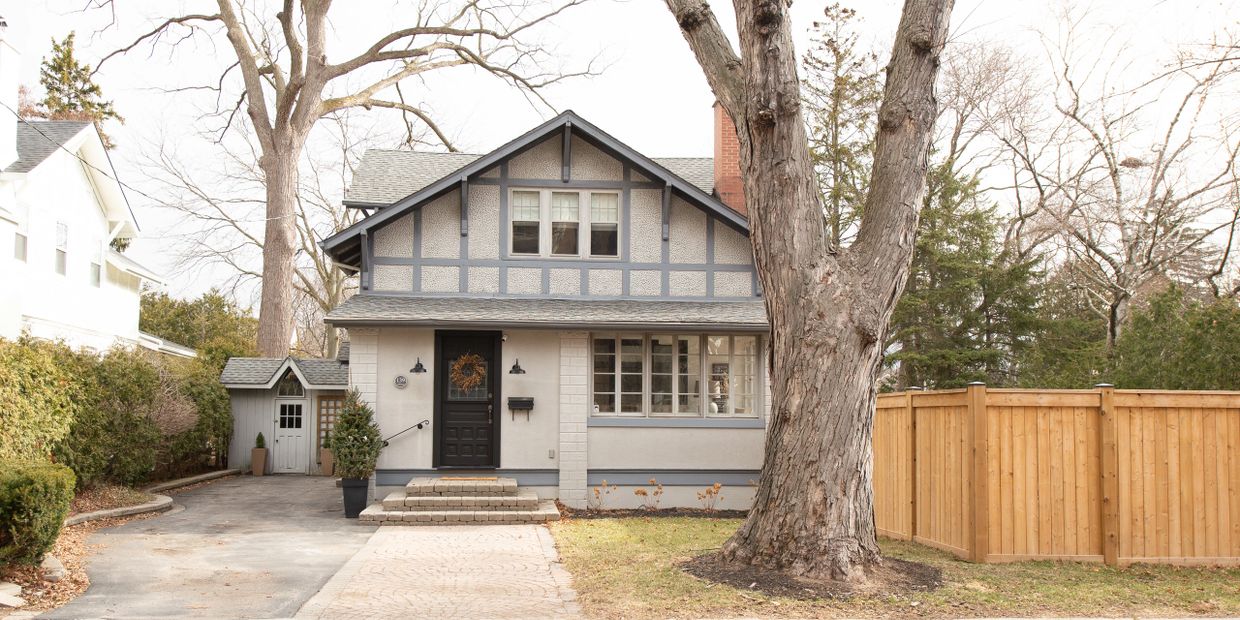 Cozy house with black door and large tree in front yard.