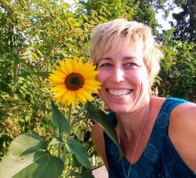 Sunshine Morse posing with a sunflower and trees in background
