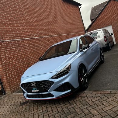 Light blue Hyundai parked in driveway beside brick wall.